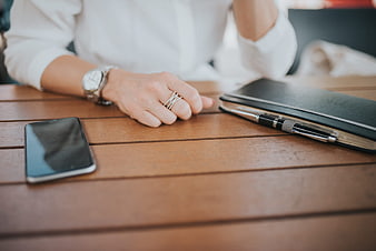 Woman's hand with watch and rings on wooden table with smartphone and notebook