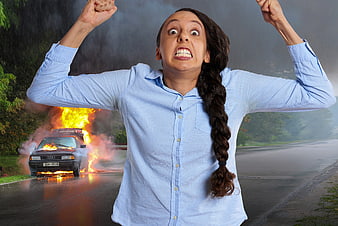 Angry woman with raised fists in front of burning car on road