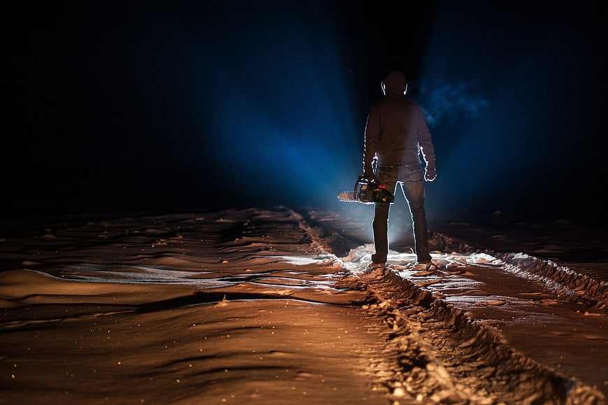 Silhouette of a person holding a chainsaw in a dark snowy landscape