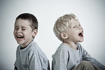 Two laughing boys sitting back to back in grey shirts