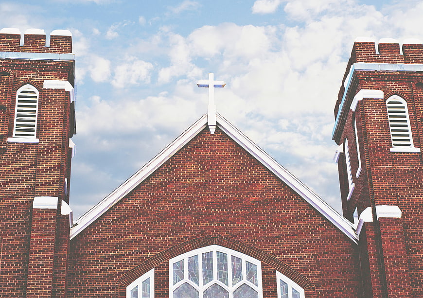 Red Brick Church Facade with White Cross and Blue Sky