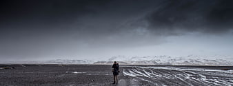 Lone Photographer in Vast Snowy Landscape Under Stormy Sky