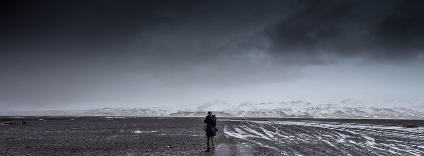 Lone Photographer in Vast Snowy Landscape Under Stormy Sky