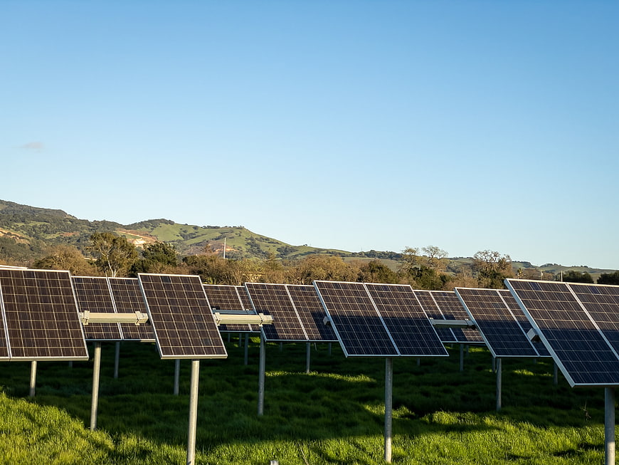 Solar panels in green field with blue sky and hills
