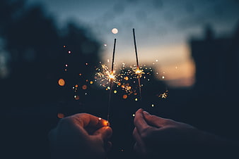 Hands holding lit sparklers against a dark twilight background