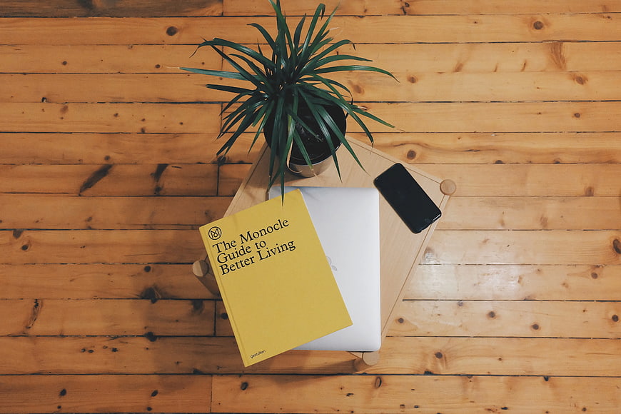 Flat lay of laptop, book, phone, and plant on wooden table