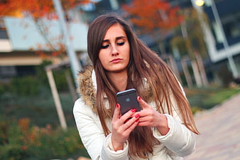 Young woman with long brown hair using smartphone outdoors in autumn