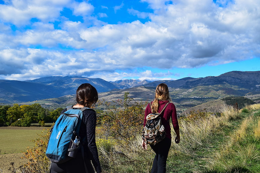 Two female hikers with backpacks overlooking mountain valley