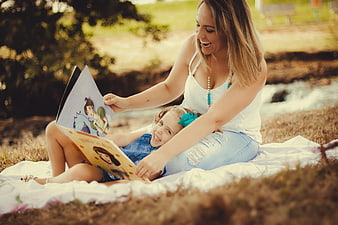 Happy mother and daughter reading book outdoors