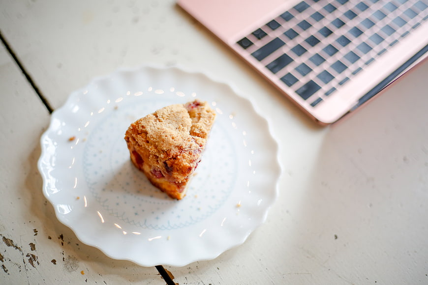 Scone on white plate with pink laptop on rustic table