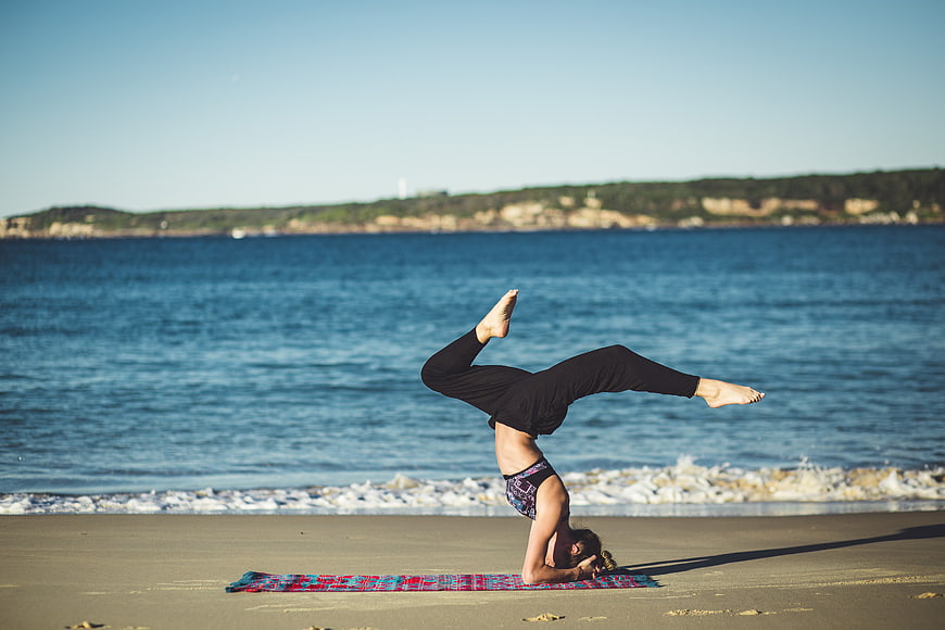 Woman performing headstand yoga pose on sandy beach