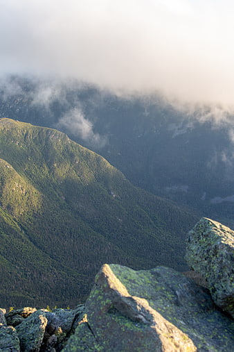 Misty Mountain Peak with Foreground Rocks and Forested Valley
