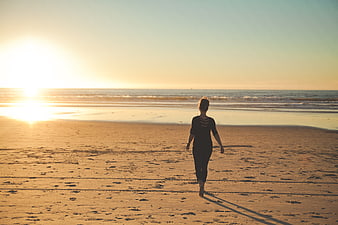 Woman Walking on Sandy Beach at Golden Sunset
