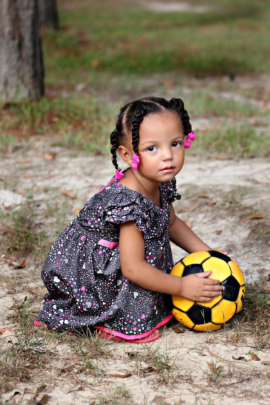 Cute Little Girl with Braids Holding Soccer Ball Outdoors