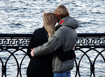 Couple embracing by waterfront railing in winter coats