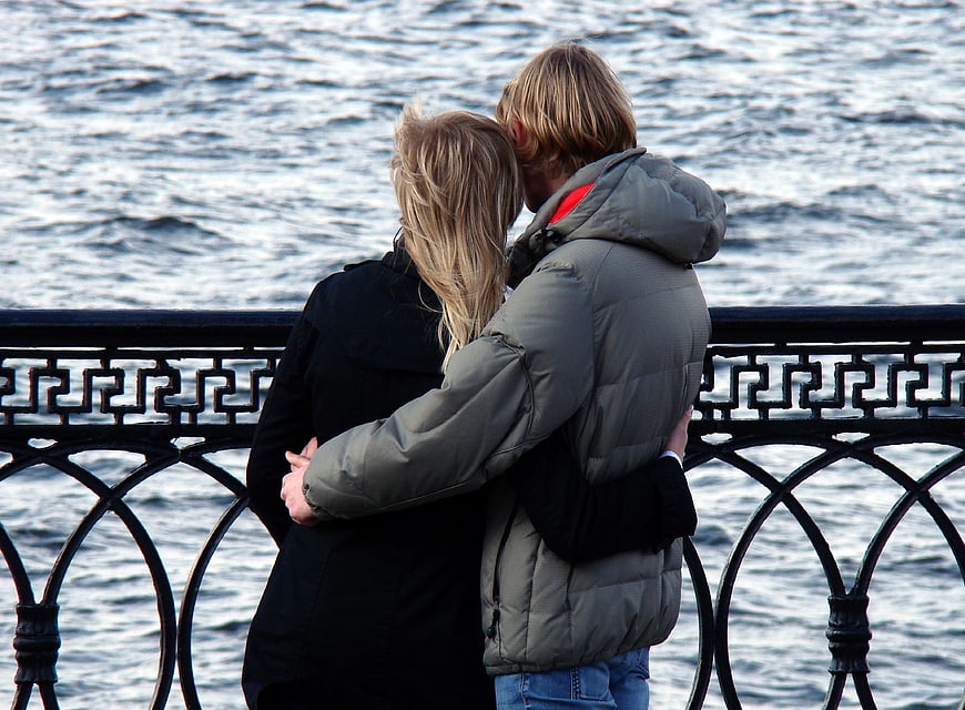 Couple embracing by waterfront railing in winter coats