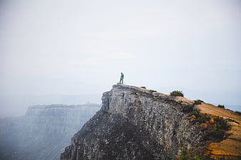 Hiker standing on rocky cliff edge in foggy mountain landscape