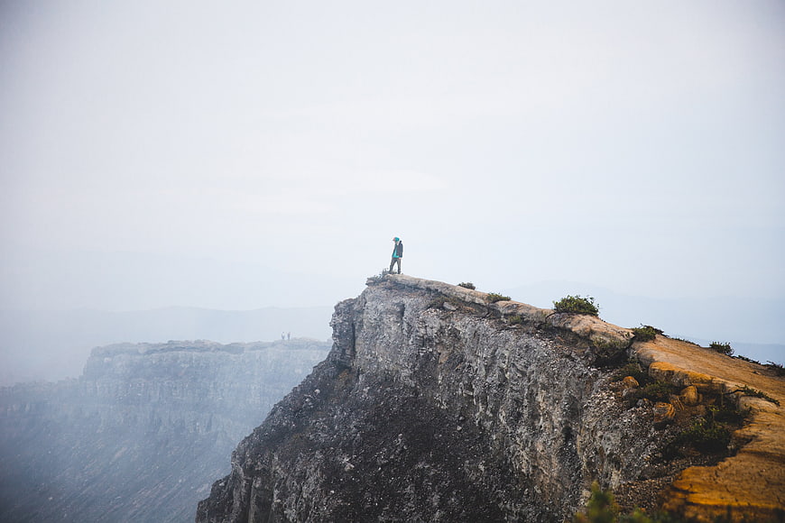 Hiker standing on rocky cliff edge in foggy mountain landscape