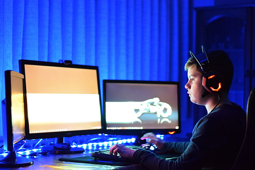 Young boy gaming on triple monitor setup with blue LED lighting