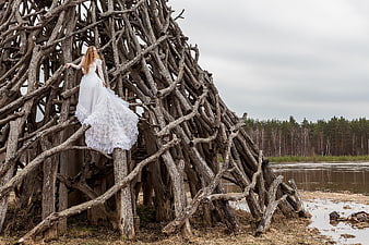 Woman in white dress climbing rustic wooden structure by lake