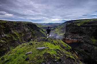 Hiker standing on mossy cliff edge overlooking dramatic canyon