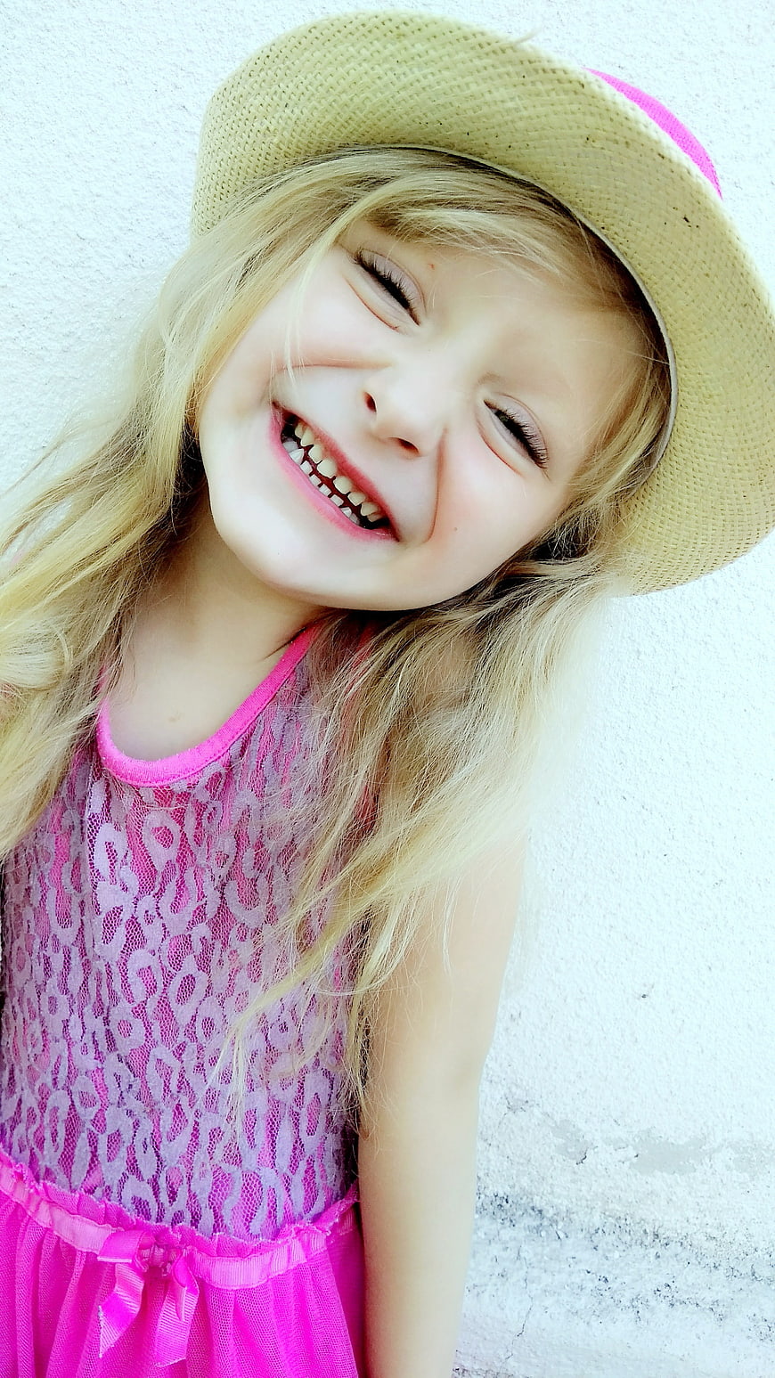 Happy blonde girl in straw hat and pink dress laughing