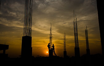 Construction workers silhouetted against dramatic sunset sky