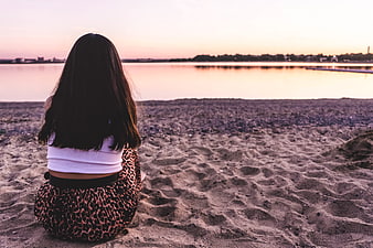 Woman Sitting on Beach Watching Sunset from Behind