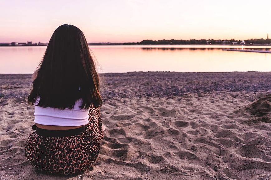 Woman Sitting on Beach Watching Sunset from Behind