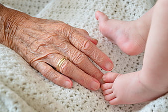 Elderly Hand Touching Baby Feet on Knitted Blanket