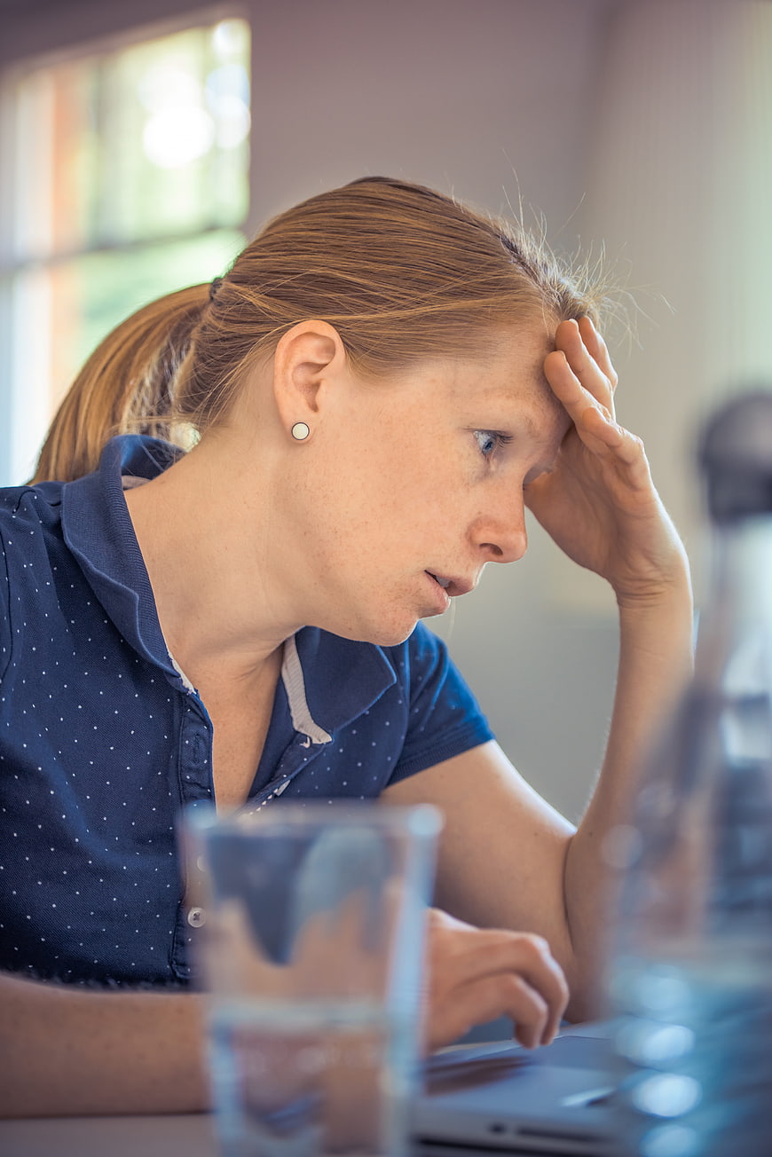 Stressed woman working on laptop with hand on forehead