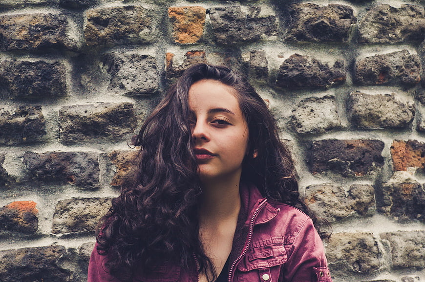 Portrait of young woman with curly hair against brick wall