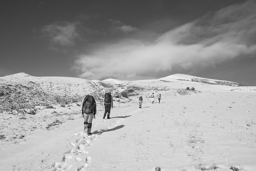 Hikers walking through snowy mountain landscape in black and white