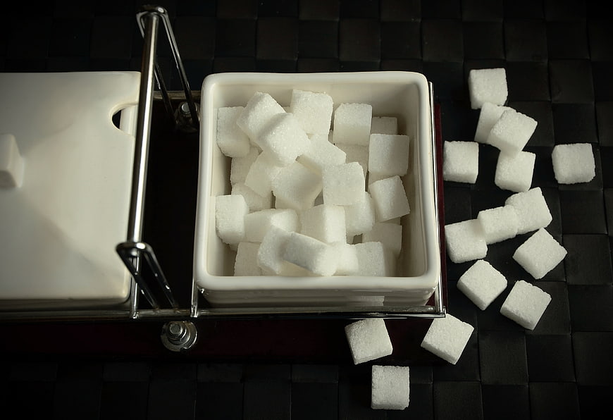 Sugar cubes in white ceramic dish on dark textured surface