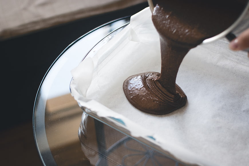 Pouring rich chocolate cake batter into a glass baking dish
