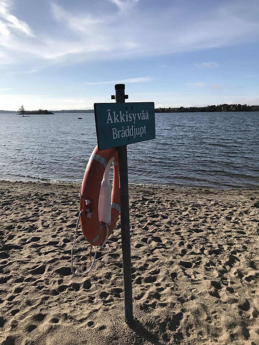 Safety sign and lifebuoy on sandy beach by lake