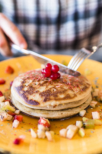 Stack of pancakes with fruit and syrup on yellow plate