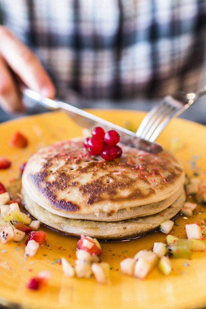 Stack of pancakes with fruit and syrup on yellow plate