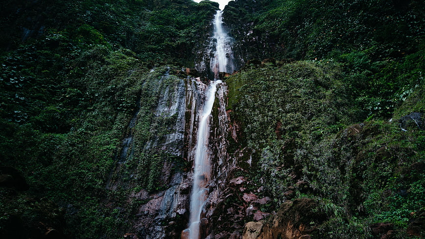 Tall waterfall cascading down lush green forest cliff