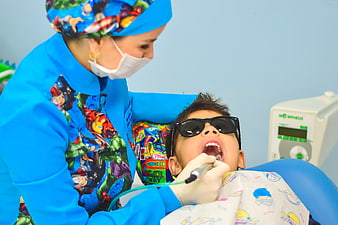Pediatric dentist examining child patient with superhero theme