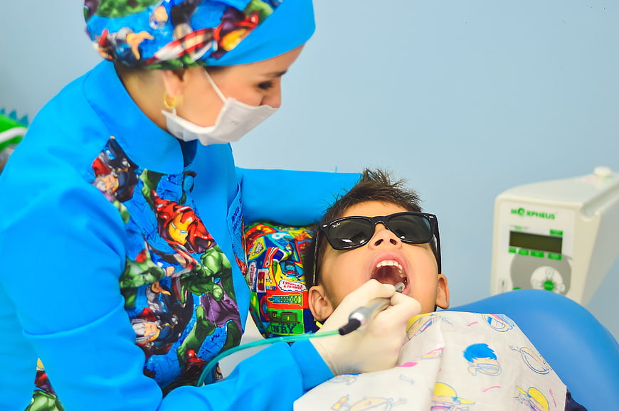 Pediatric dentist examining child patient with superhero theme