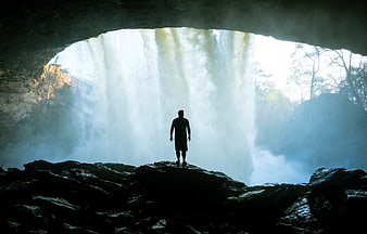 Silhouette of Man Standing in Cave Behind Waterfall