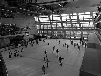 Black and white wide shot of people ice skating in a modern indoor rink