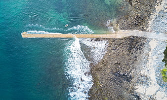 Aerial view of concrete pier extending into turquoise ocean waves
