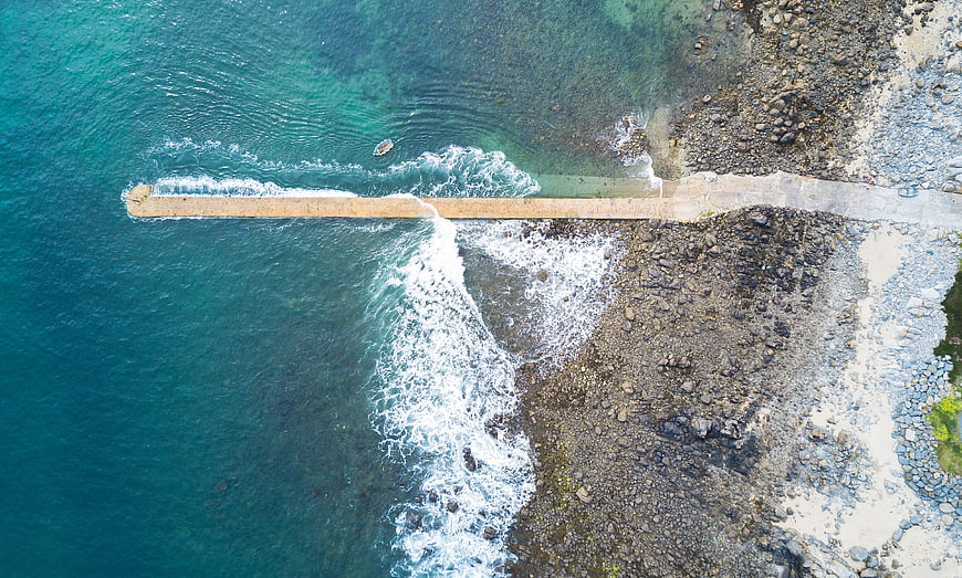 Aerial view of concrete pier extending into turquoise ocean waves