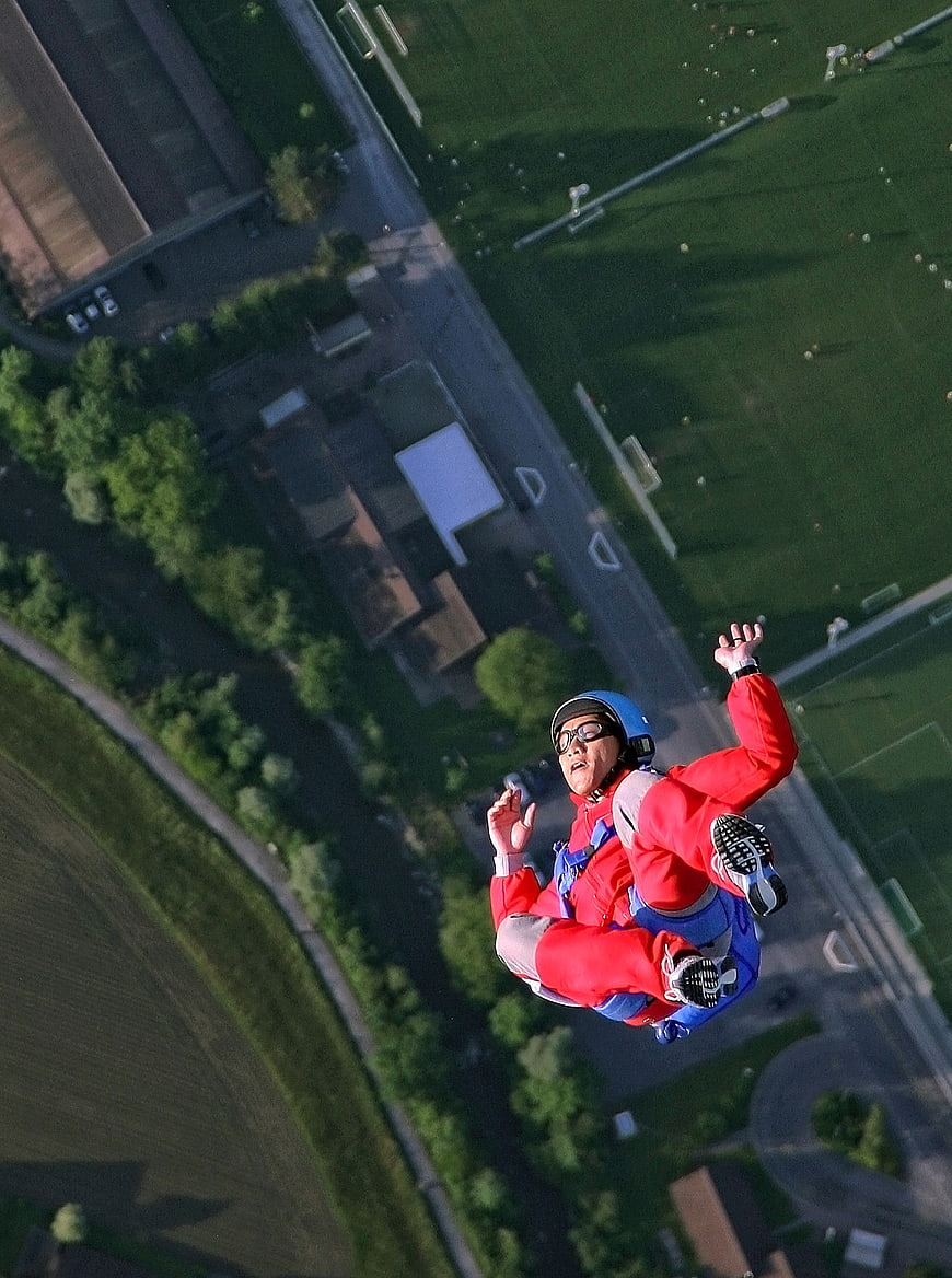 Skydiver in Red Suit Freefalling Over Green Landscape