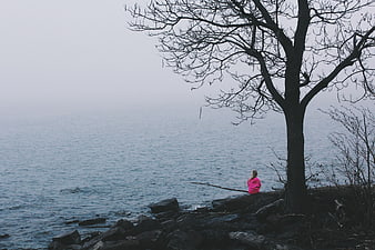 Girl in Pink Sitting by Foggy Lake Under Bare Tree