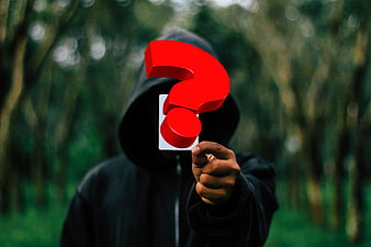 Anonymous hooded figure holding red question mark in forest