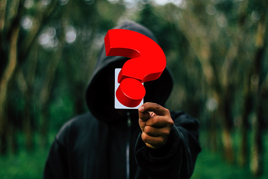 Anonymous hooded figure holding red question mark in forest