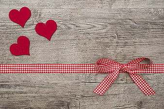Red felt hearts and gingham ribbon on rustic wood background
